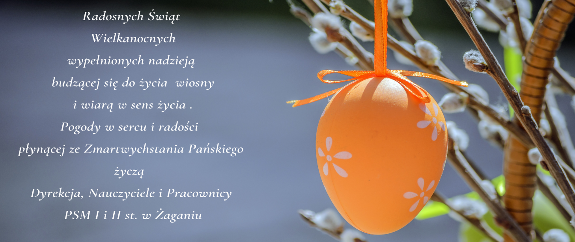 Na ciemnoszarym tle w centrum wisi pomarańczowa pisanka, za nią znajdują się bazie. Po lewej stronie umieszczono tekst życzeń z okazji Świąt Wielkiej Nocy od Dyrekcji, Nauczycieli i PSM I i II stopnia w Żaganiu. 
