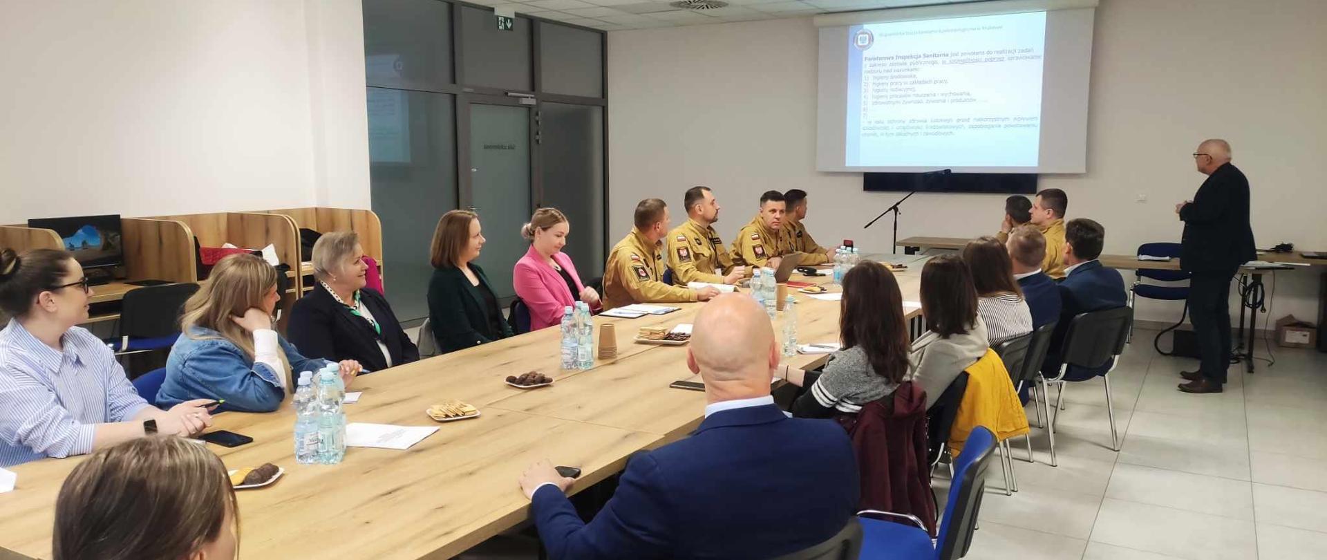 na zdjęciu uczestnicy szkolenia przy stole ma sali szkoleniowej. W dalszej części prezentacja multimedialna.