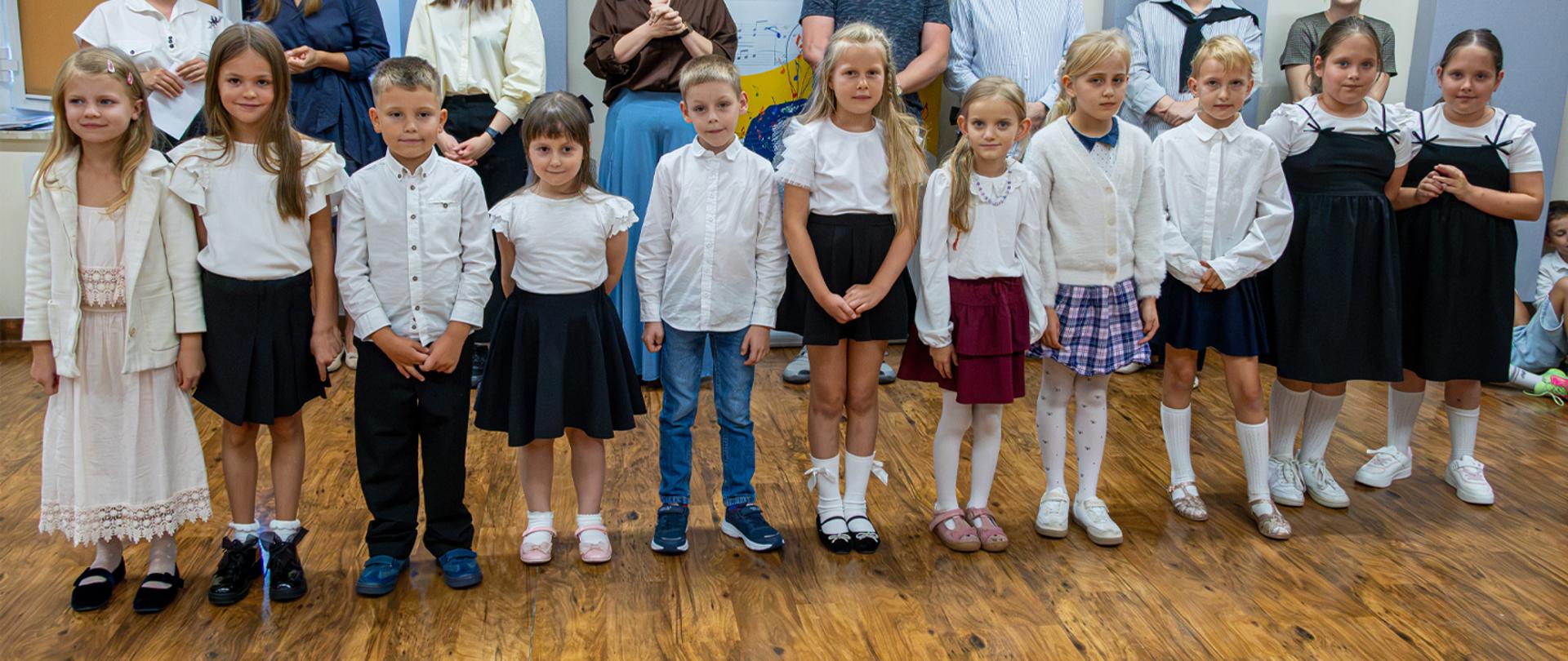 Na zdjęciu grupa kilkunastu młodych uczniów stoi w auli szkolnej.