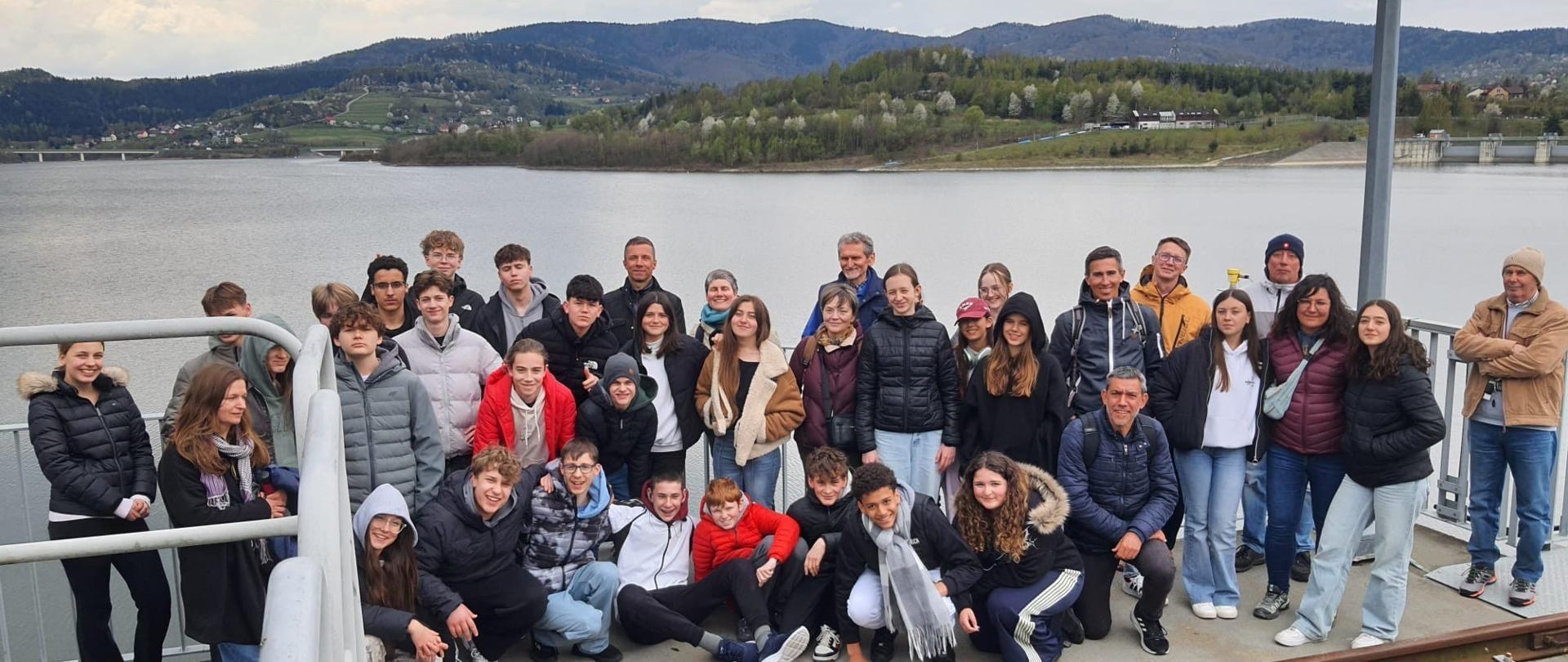 Zdjęcia, na którym znajduje się grupa uczniów Dwujęzycznej Szkoły Podstawowej nr 1 w Warszawie, w tle Zbiornik Wodny Świnna Poręba. 