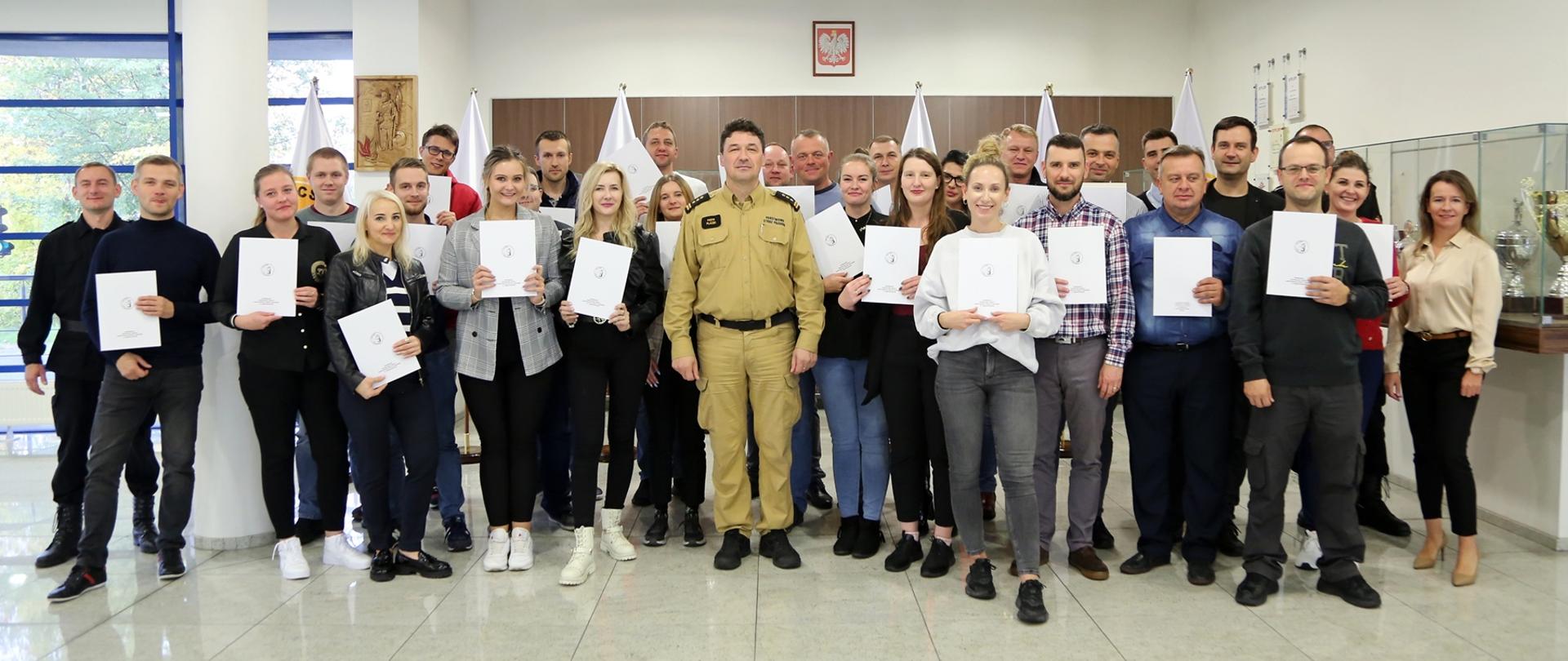 Grupowe zdjęcie uczestników szkolenia w towarzystwie Komendanta Centralnej Szkoły PSP, trzech funkcjonariuszy CS PSP i kobiety