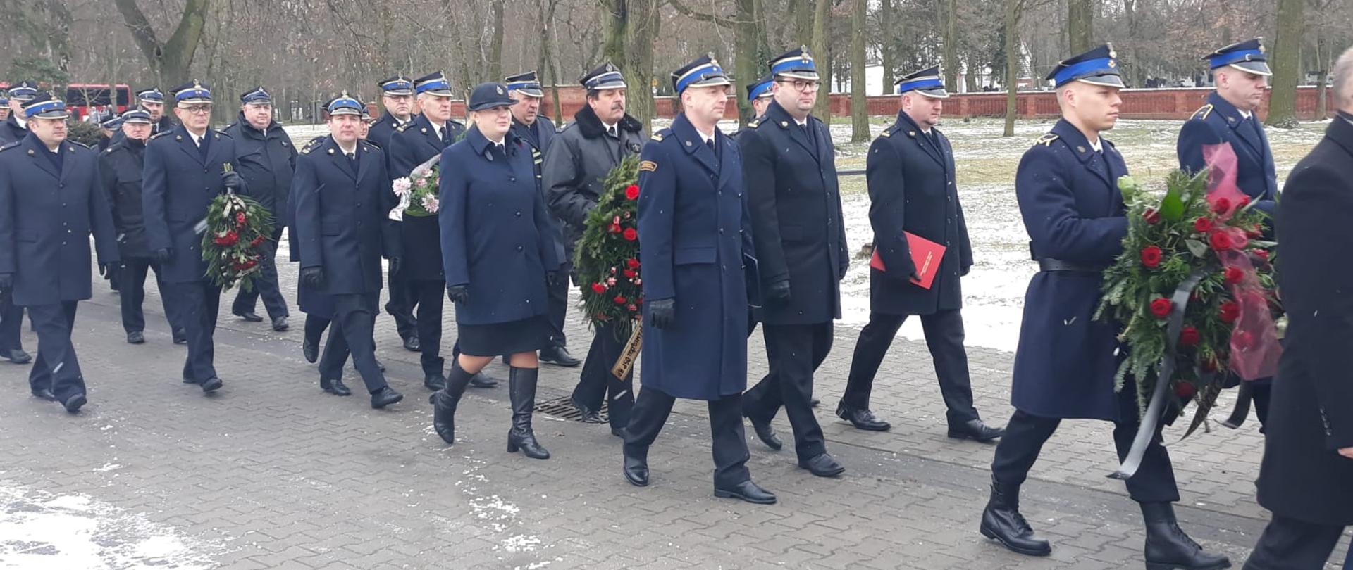 kondukt żałobny złożony ze strażaków, niektórzy noiosą wieńce, zima