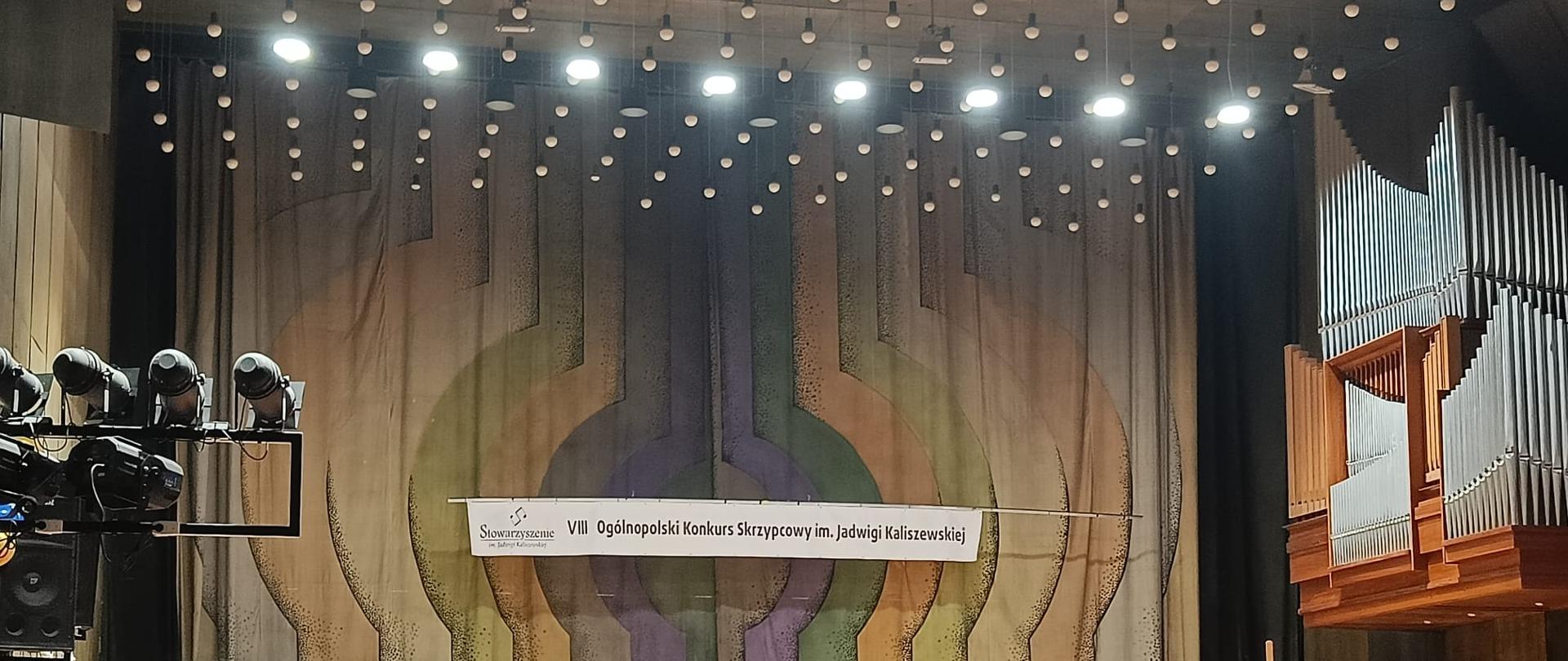 Na zdjęciu Katarzyna Kurczewska podczas występu na VIII Ogólnopolskim Konkursie Skrzypcowym im. Jadwigi Kaliszewskiej. Uczennica stoi na na scenie w Sali Koncertowej Poznańskiej Ogólnokształcącej Szkoły Muzycznej II stopnia im. M. Karłowicza w Poznaniu, przy ul.Solnej 12. Obok uczennicy po prawej stronie przy fortepianie siedzi pianista towarzyszący podczas występu. U góry baner z napisem VIII Ogólnopolski Konkurs Skrzypcowy im. Jadwigi Kaliszewskiej