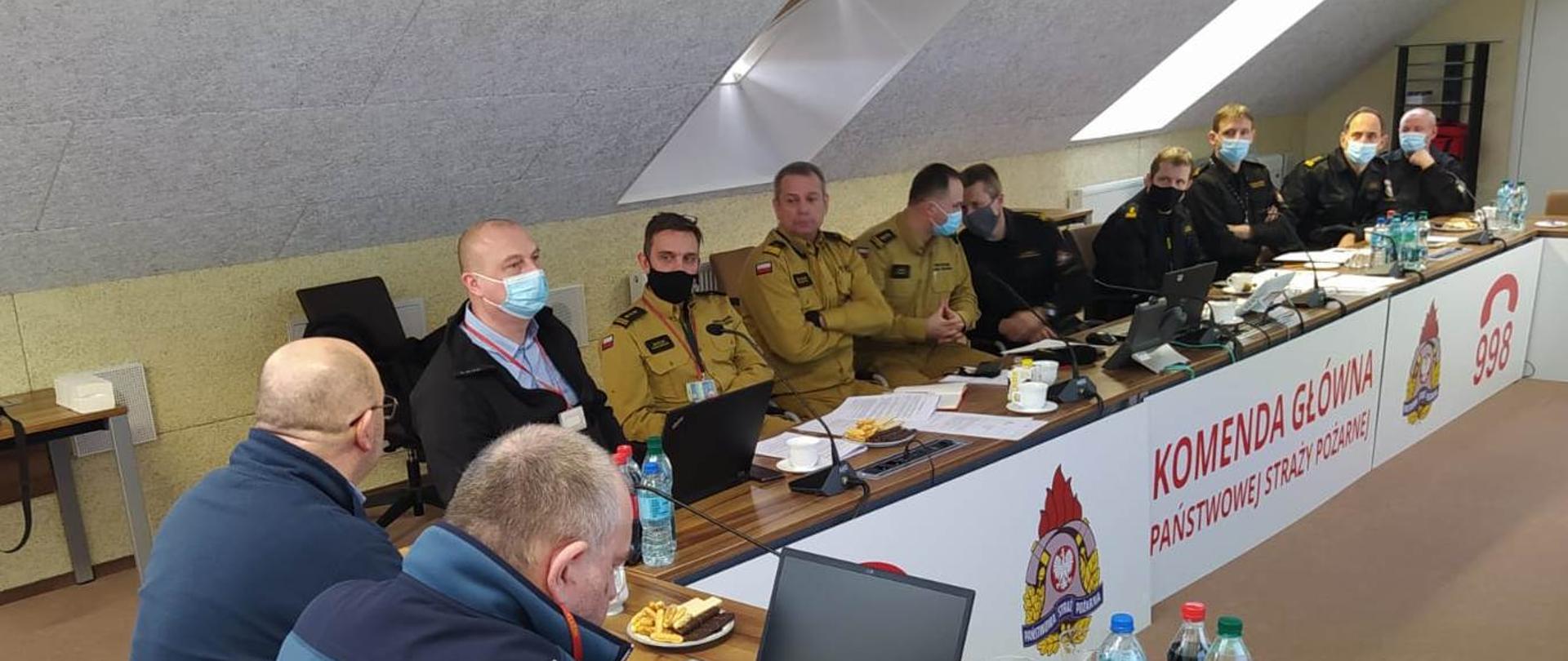 Uczestnicy spotkania siedzą przy biurku w kształcie litery U, na przodzie widnieje napis KOMENDA GŁÓWNA PSP