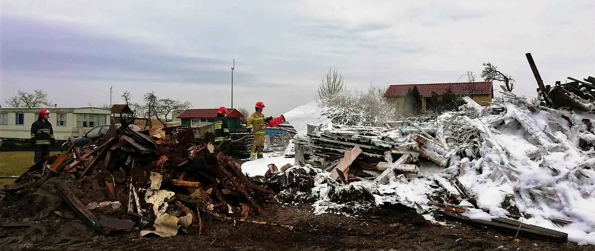 Strażacy dogaszają pogorzelisko pianą gaśniczą.