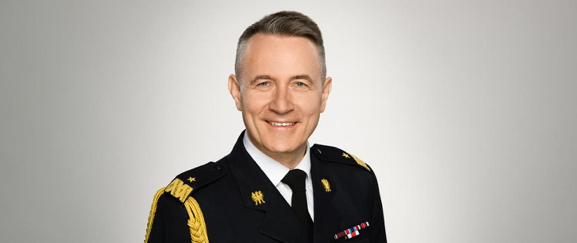 Zdjęcie przedstawia nadbryg. Andrzeja Bartkowiaka w czarnym mundurze galowy ze złotym stopniem na pagonach, sznurem oraz orłami na kapie.