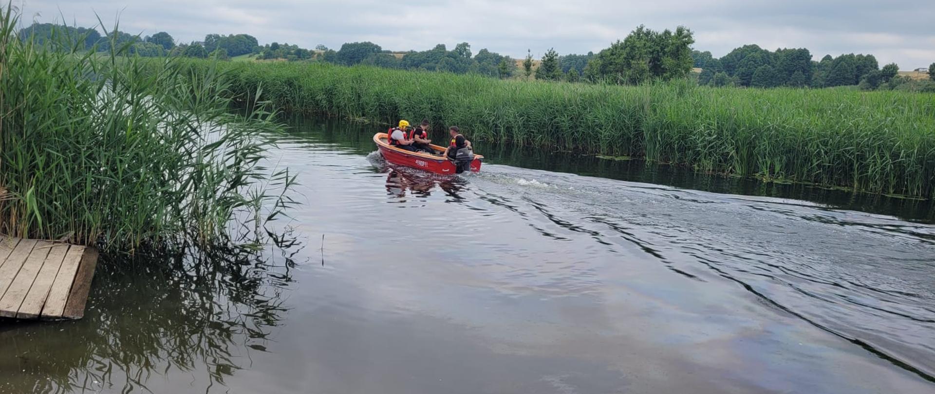 Tafla wody rzeki Brda, widoczne czcinowiska. Na tafli wody łódka straży pożarnej a na niej strażacy. 