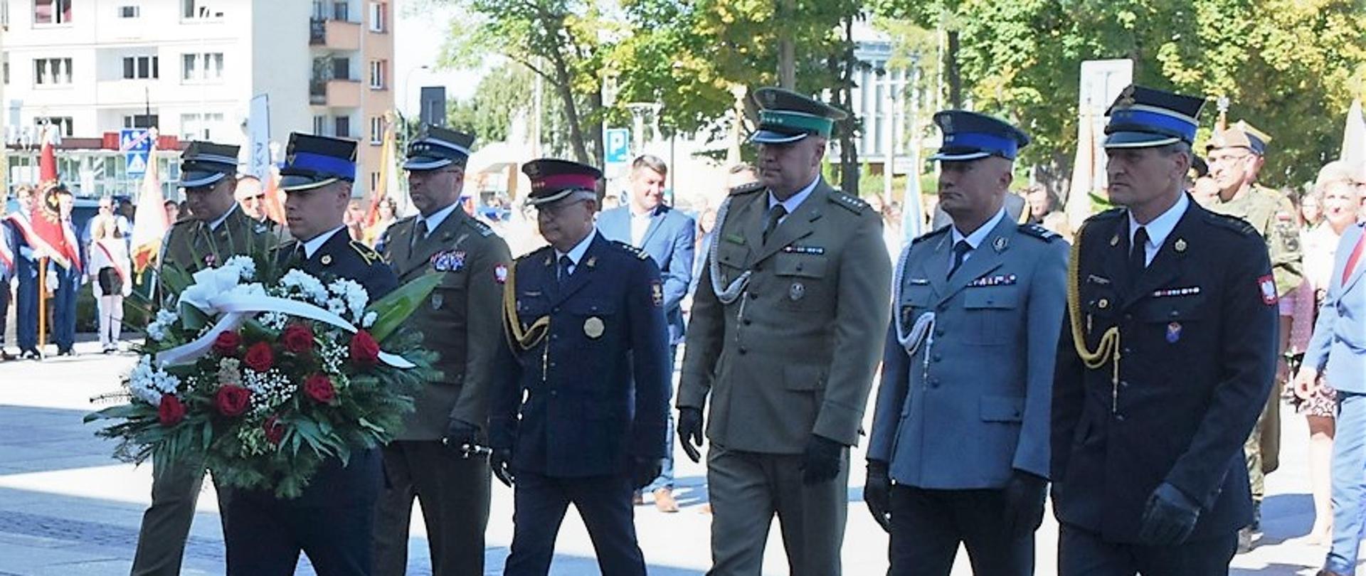 Zdjęcie przedstawia złożenie wieńca pod tablicą upamiętniającą wrześniową obronę Westerplatte z 1939 r. Wieniec składają przedstawiciele służb mundurowych wśród nich Komendant Miejski Państwowej Straży Pożarnej w Kielcach bryg Mariusz Góra.
