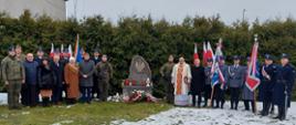 Na częściowo zaśnieżonej trawie na tle krzyży stoi grupka osób. Wśród nich mundurowi, księża.