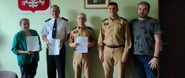 W szeregu od lewej strony stoją Pani wójt Brzezin Barbara Hojnacka, prezes jednostki Ochotniczej Straży Pożarnej w Poliku druh Piotr Kaczmarek, Komendant Powiatowy Państwowej Straży Pożarnej starszy brygadier Mariusz Kaczmarski, naczelnik jednostki Ochotniczej Straży Pożarnej w Poliku dr Erwin Mospinek, pracownik Urzędu Gminy Brzeziny Konrad Lenkiewicz. Komendant, Pni Wójt i Prezes jednostki prezentują przed sobą podpisane porozumienie o włączeniu jednostki Polik do krajowego systemu ratowniczo gaśniczego. Sytuacja ma miejsce w gabinecie Pani Wójt. Na ścianie za pozującymi do zdjęcia widać godło polski krzyż i obraz. 