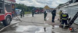 strażacy podczas działań gaśniczych przy budynku dyskontu spożywczego, w tle auta bojowe