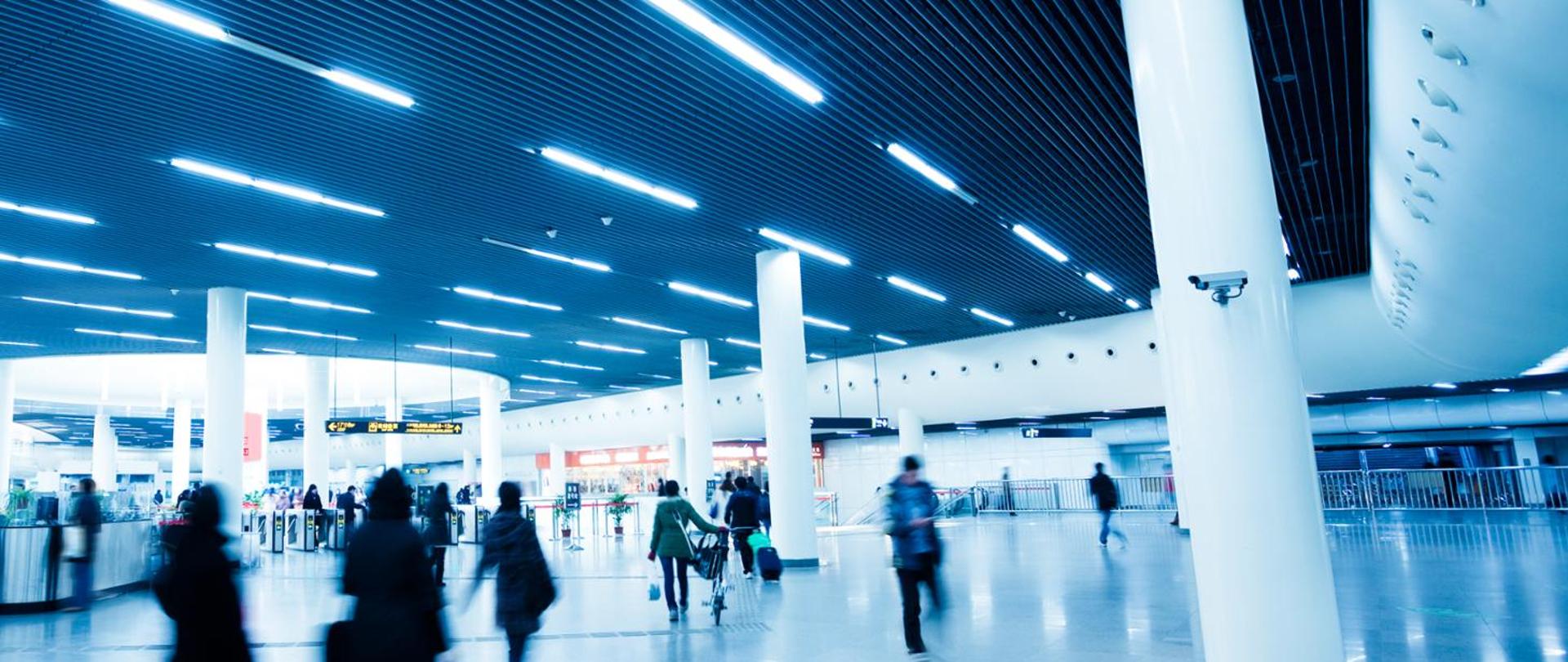 Jasno oświetlony terminal lotniska z przechodzącymi podróżnymi.
