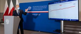 Wojewoda Mikołaj Bogdanowicz podczas konferencji prasowej. Na ekranie wykres obrazujący przyrost ilości pacjentów w kujawsko-pomorskich szpitalach