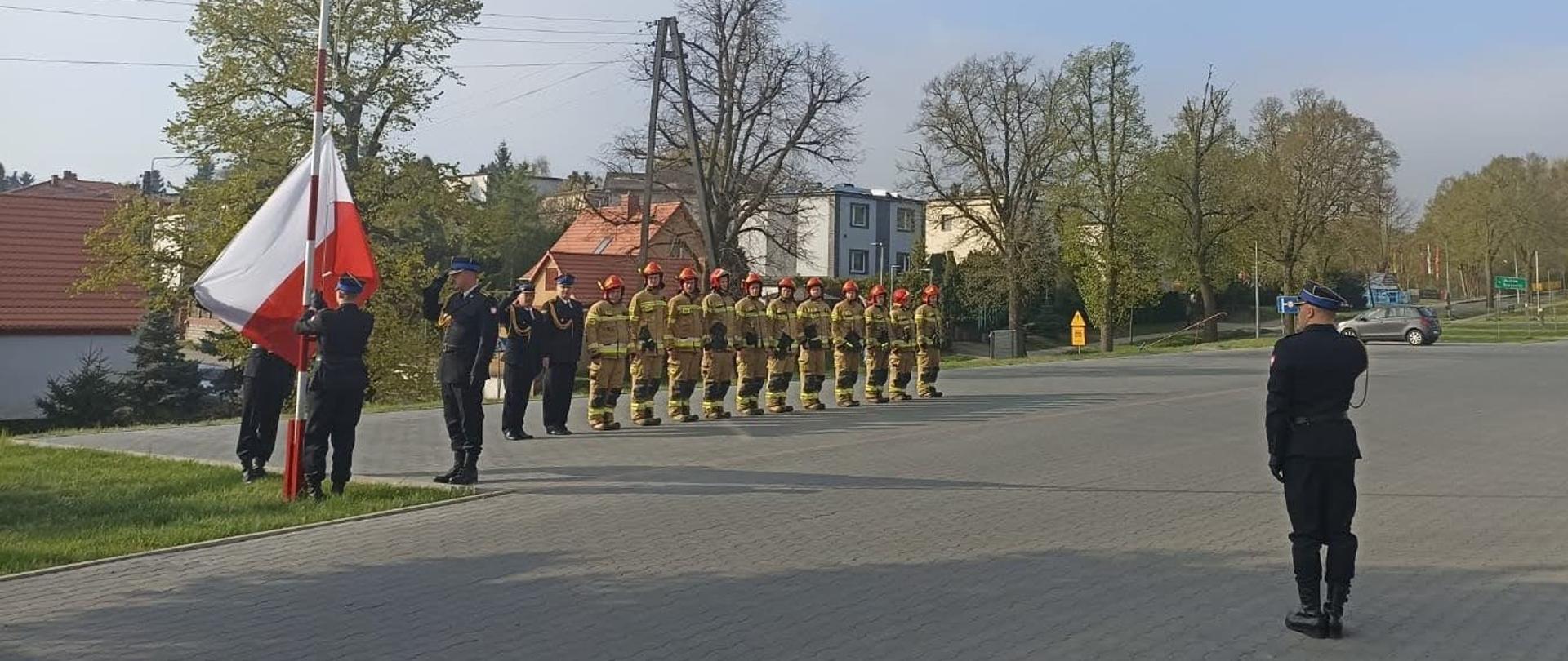 Uroczyste podniesienie flagi państwowej, zdjęcie wykonano przy maszcie flagowym na terenie KP PSP w Chełmnie. Na zdjęciu znajduje się zmiany służbowe podczas podnoszenia flagi państwowej.
