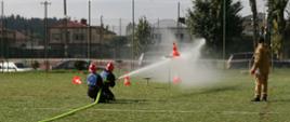 Zdjęcie przedstawia moment przebiegu konkurencji ćwiczenie bojowe przez męską drużynę pożarniczą podczas VIII Powiatowych Zawodów Sportowo-Pożarniczych Ochotniczych Straży Pożarnych powiatu gołdapskiego (zrzucenie pachołków z podstaw prądami wody)