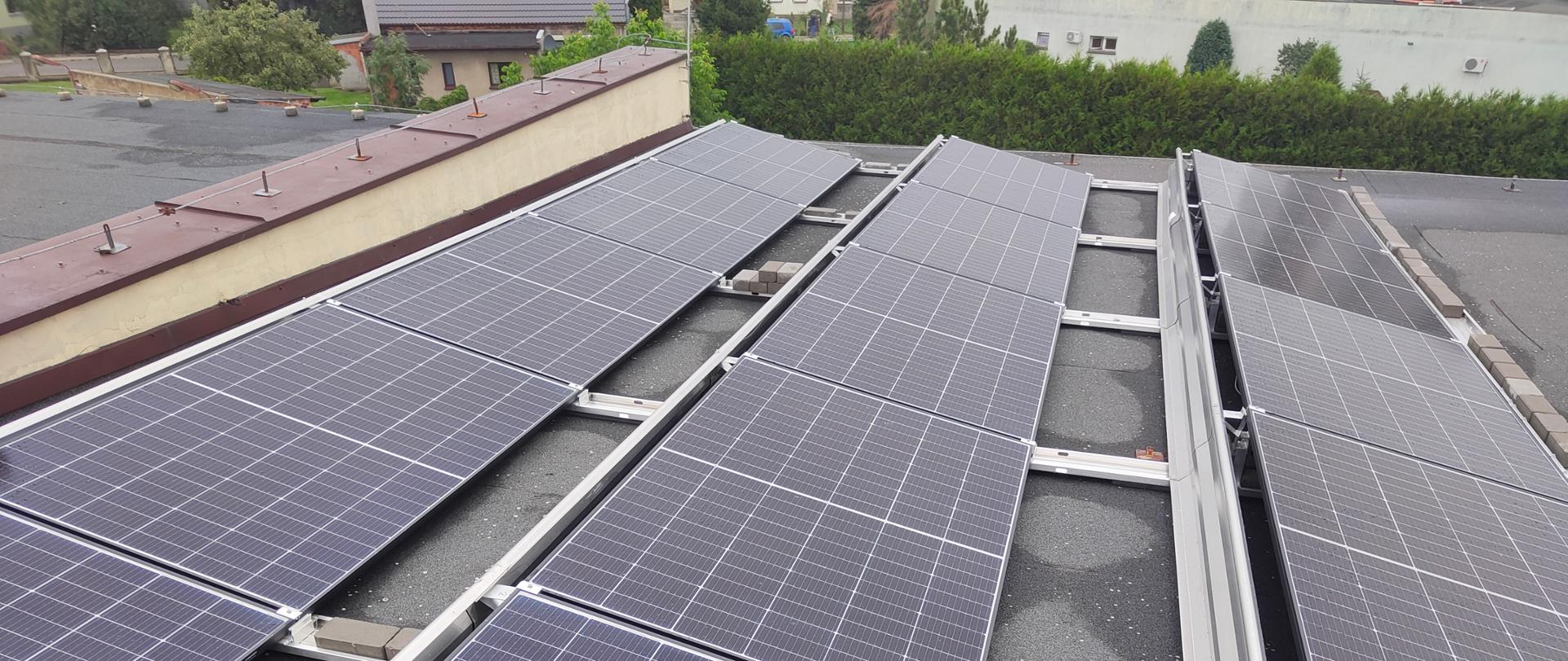 Ogniwa fotowoltaiczne zamontowane na dachu komendy straży pożarnej. Ogniwa umieszczone na listwach aluminiowych ułożonych na dachu pokrytym papą termozgrzewalną. 