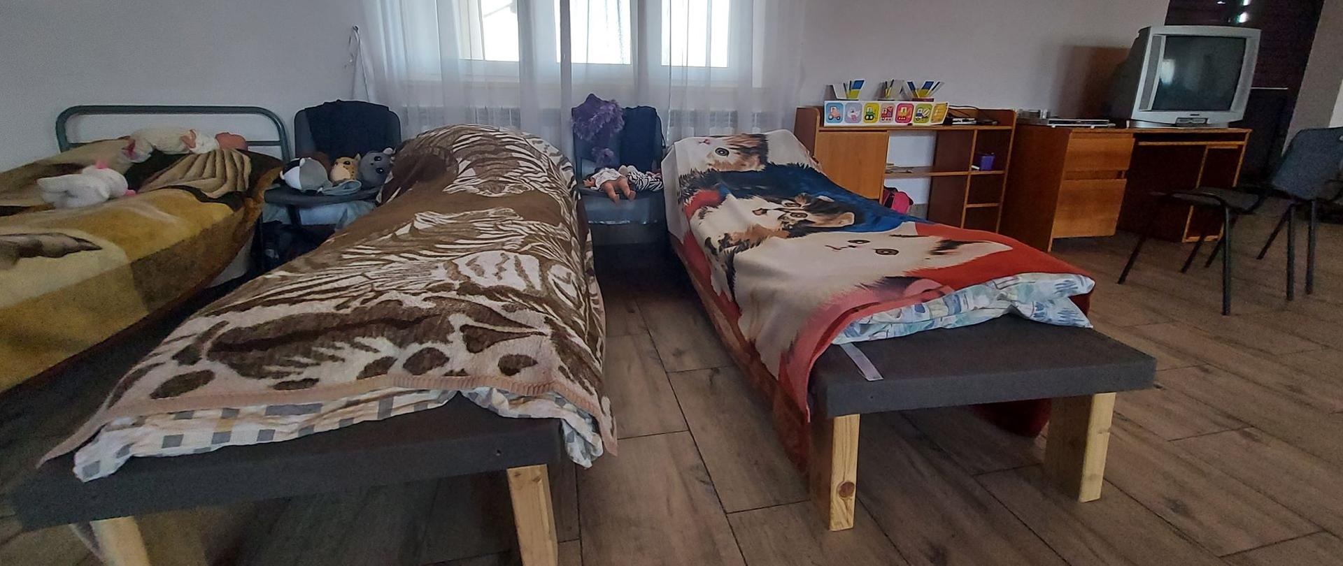 Na zdjęciu sala przygotowana do przyjęcia uchodźców. Wyposażenie sali: łóżka, wieszaki, biurko, telewizor itp.