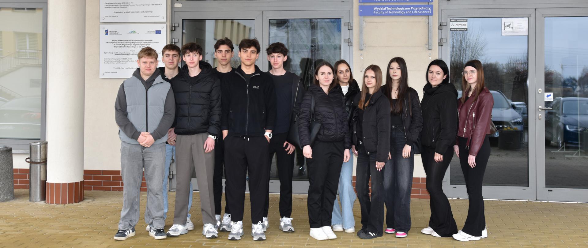 Na zdjęciu widoczna grupa młodzieży stojąca pod budynkiem gmachu Wydziału Technologiczno-Przyrodniczego Uniwersytetu Rzeszowskiego.