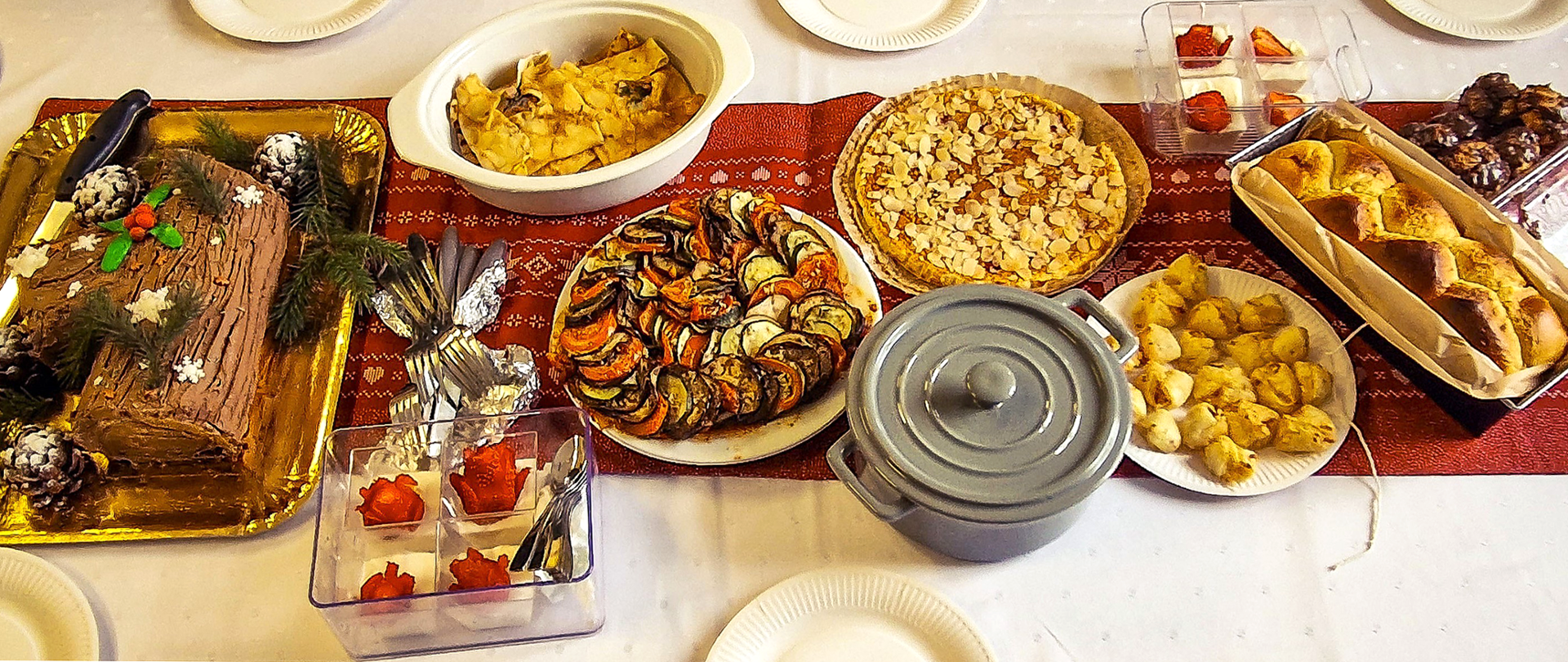 Na stole, na bieżniku stoją talerze i półmiski zdaniami kuchni francuskiej; są ciasta i Dania z warzyw