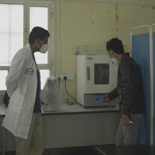 Dwóch mężczyzn stoi przy urządzeniu do prowadzenia badań. Obok ustawiono niebieski parawan.