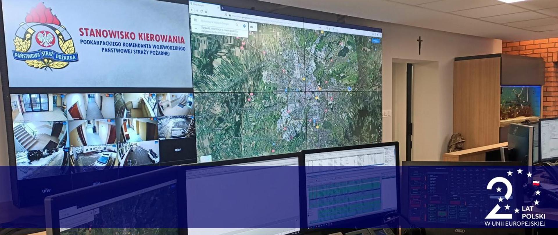 Zdjęcie stanowiska kierowania podkarpackiego komendanta wojewódzkiego PSP. Na fotografii monitory komputerowe oraz monitory nadzoru wizyjnego. W prawym dolnym rogu logotyp 20 lat Polski w Unii Europejskiej.