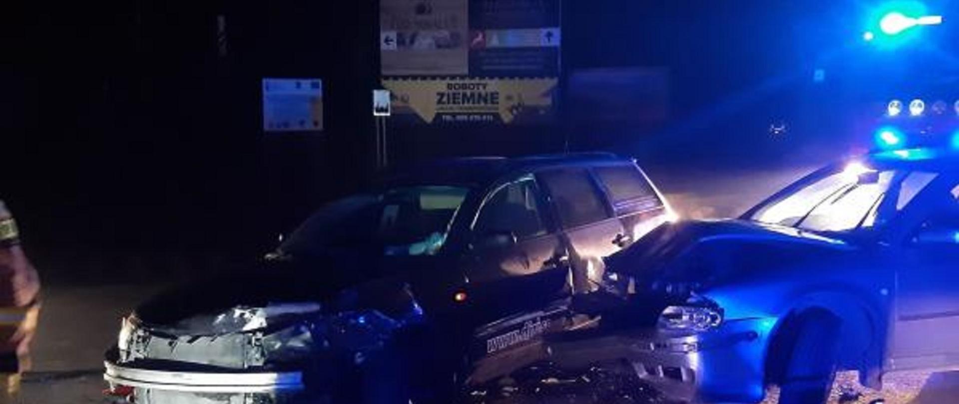 Zdjęcie przedstawia zderzenie dwóch samochodów osobowych w Zakopanem na drodze krajowej nr 47. Zdjęcie zostało wykonane w godzinach wieczornych. W tle reklamy oraz wóz strażacki z Jednostki ratowniczo-gaśniczej w Zakopanem.