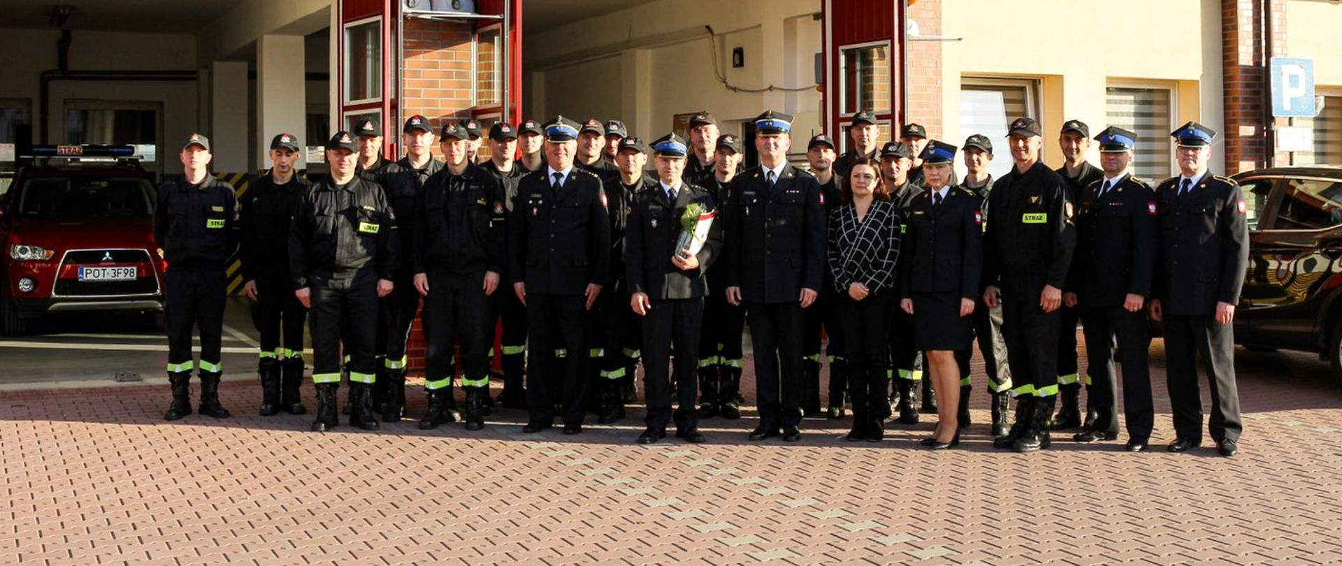 Grupa strażaków stoi na placu manewrowym przed strażnicy