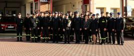 Grupa strażaków stoi na placu manewrowym przed strażnicy