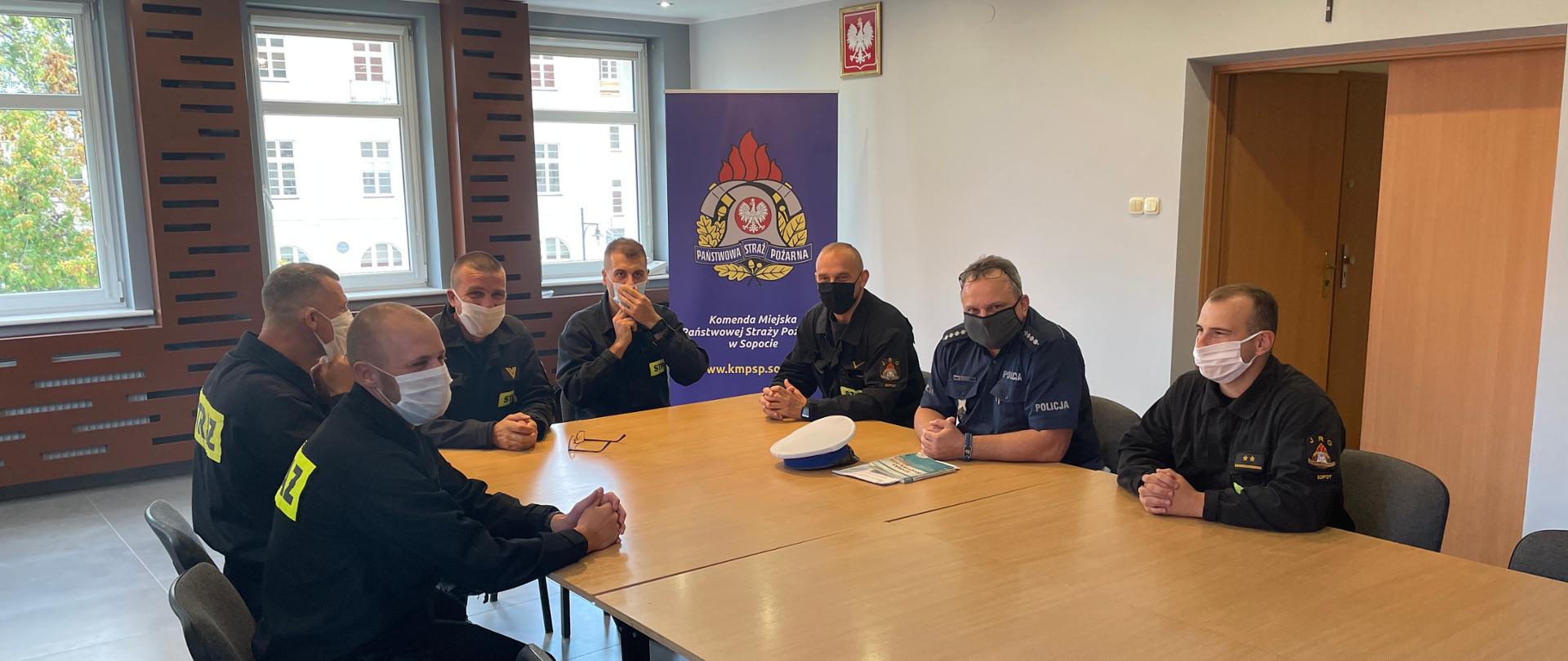 Strażacy siedzący na świetlicy podczas szkolenia słuchaja policjanta, który omawia zmiany w przepisach ruchu drogowego