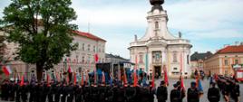 Widok z tyłu. Poczty sztandarowe OSP oraz pododdziały strażackie w szyku w trakcie uroczystości. W tle bazylika Ofiarowania Najświętszej Maryi Panny. 