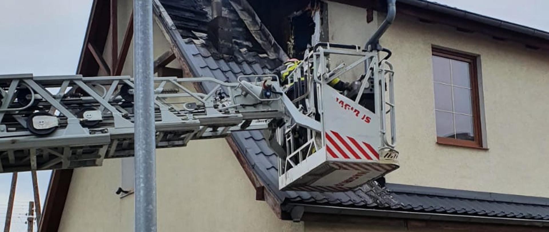 kosz drabiny pożarniczej nad dachem palącego się budynku otoczonego betonowym płotem, pofałdowane poszycie dachu