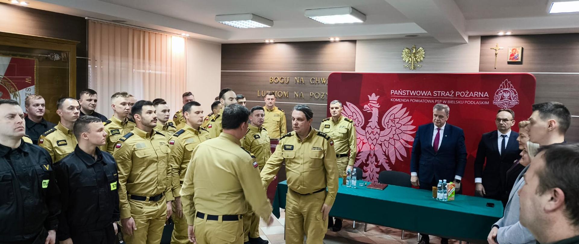 19 lutego 2026 r. w sali konferencyjnej Komendy Powiatowej PSP w Bielsku Podlaskim odbyła się narada podsumowująca funkcjonowanie ochrony przeciwpożarowej na terenie powiatu bielskiego za 2025 rok - zastępca podlaskiego komendanta wojewódzkiego PSP wita się z dowódcą uroczystości, w tle strażacy i zaproszeni goście