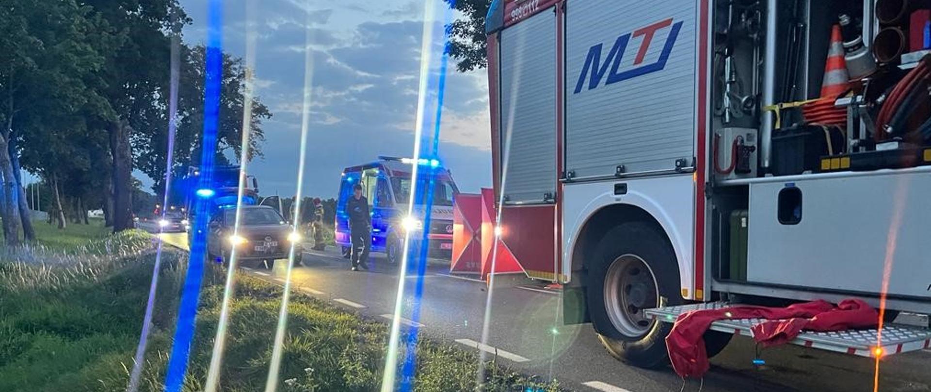 Zdjęcie przedstawia pojazd pożarniczy oraz karetkę pogotowia ratunkowego podczas działań ratowniczych. 