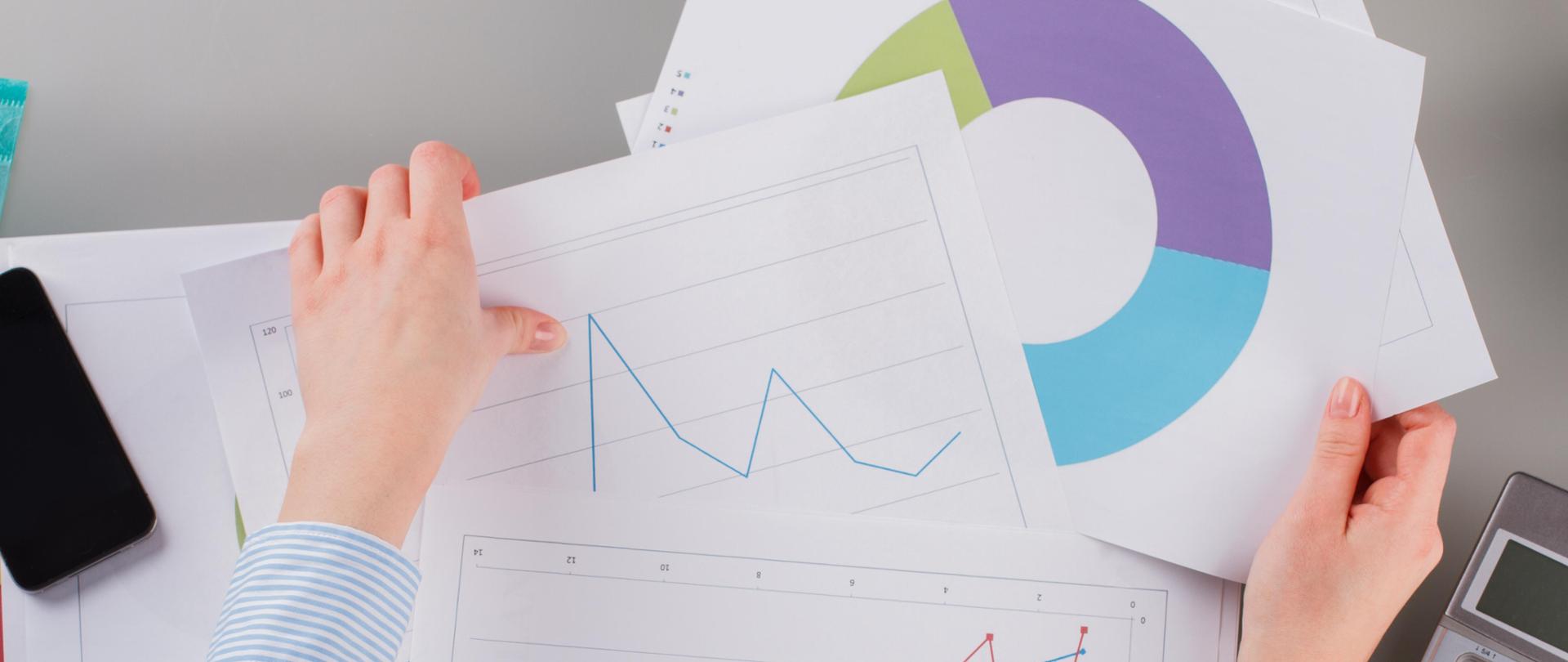 Trader woman working at office close up. Hands of business woman holding graphs while sitting at table in office.
