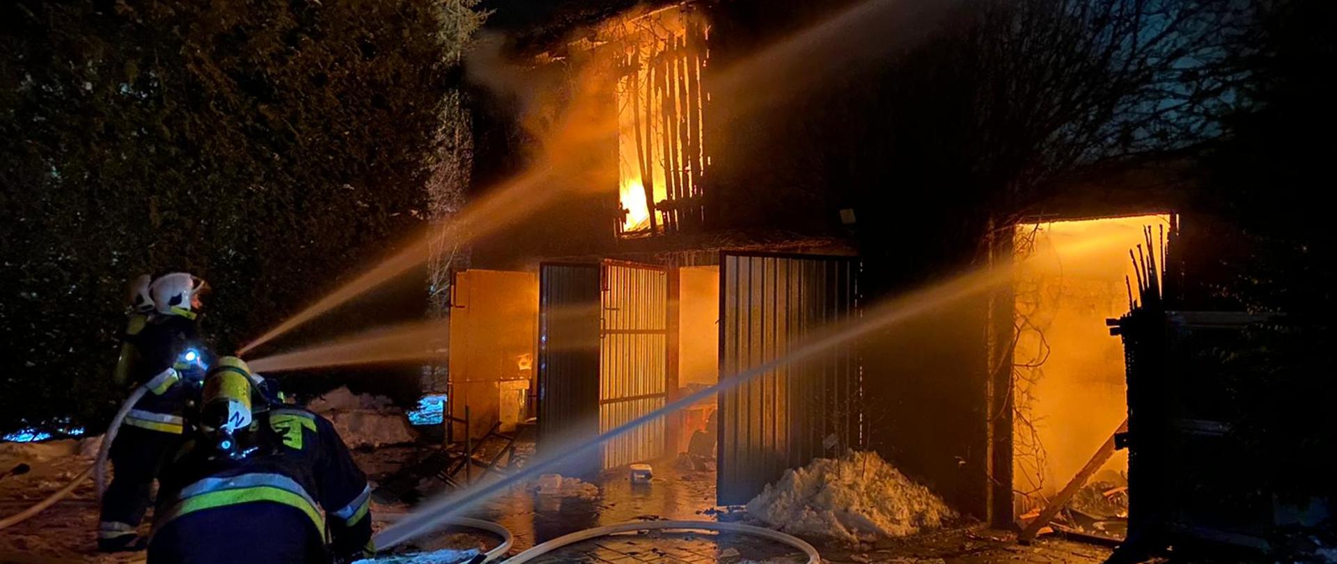 Strażacy podający prądy gaśnicze w natarciu na palący się budynek gospodarczy