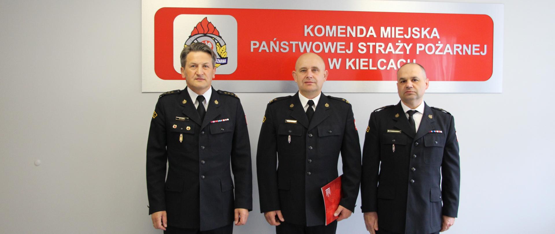 Od lewej stoją; Komendant Miejski PSP w Kielcach st. bryg. Mariusz Góra, nowy dowódca Jednostki Ratowniczo-Gaśniczej Nr 4 w Chmielniku mł. bryg. Paweł Młynarski i Zastępca Komendanta Miejskiego PSP w Kielcach bryg. Piotr Wieczorek