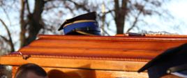 Widok na trumnę niesioną w kondukcie pogrzebowym. Na wieku czapka.
