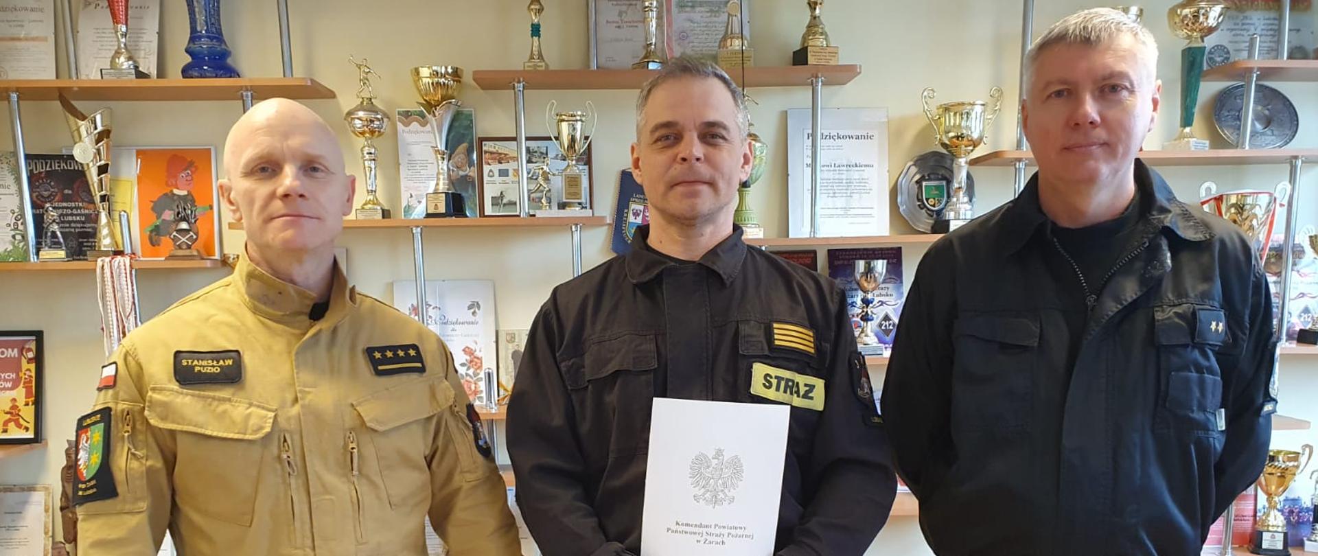 Na zdjęciu widoczny jest strażak wyróżniony nagrodą w obecności Dowódcy JRG i Dowódcy zmiany 