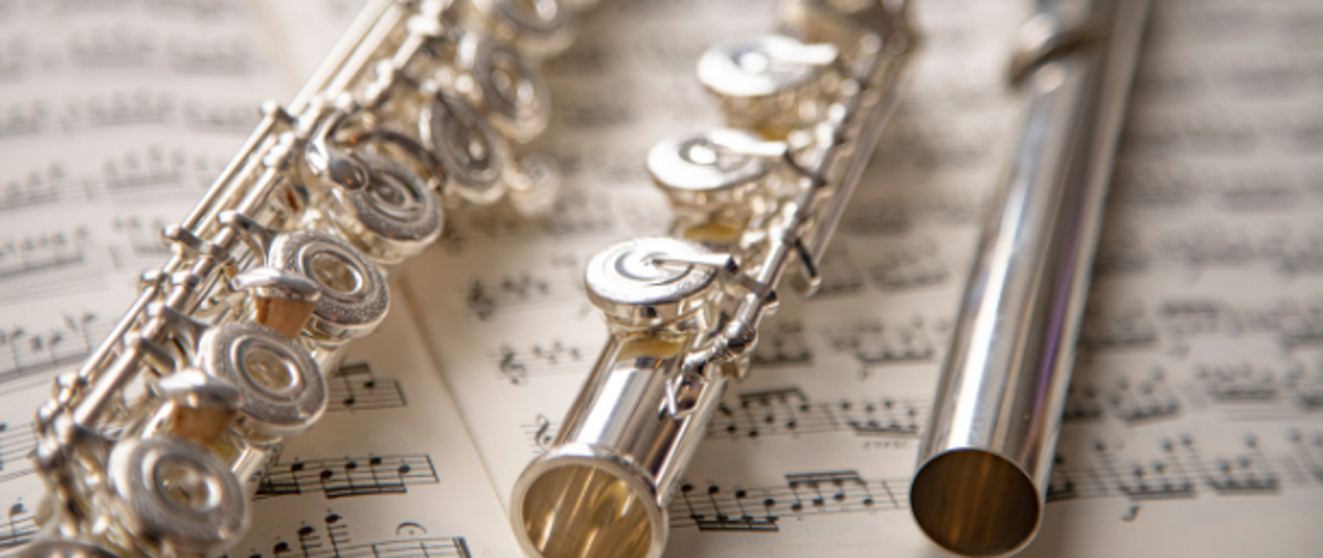 Fotografia przedstawia flet w trzech częściach rozłożony na zapisanych nutach