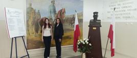 Dwie osoby stoją przed obrazem z Józefem Piłsudskim na koniu, obok polskich flag i popiersia.