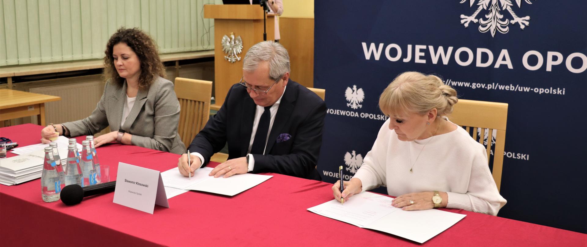 Mężczyzna i dwie kobiety podpisujące dokument