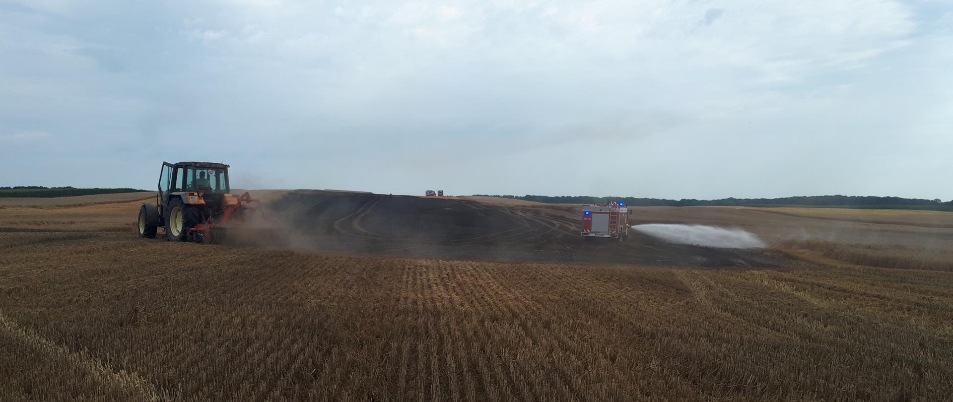 Zdjęcie przedstawia pogorzelisko pożaru ścierniska oraz ciągnik rolniczy.