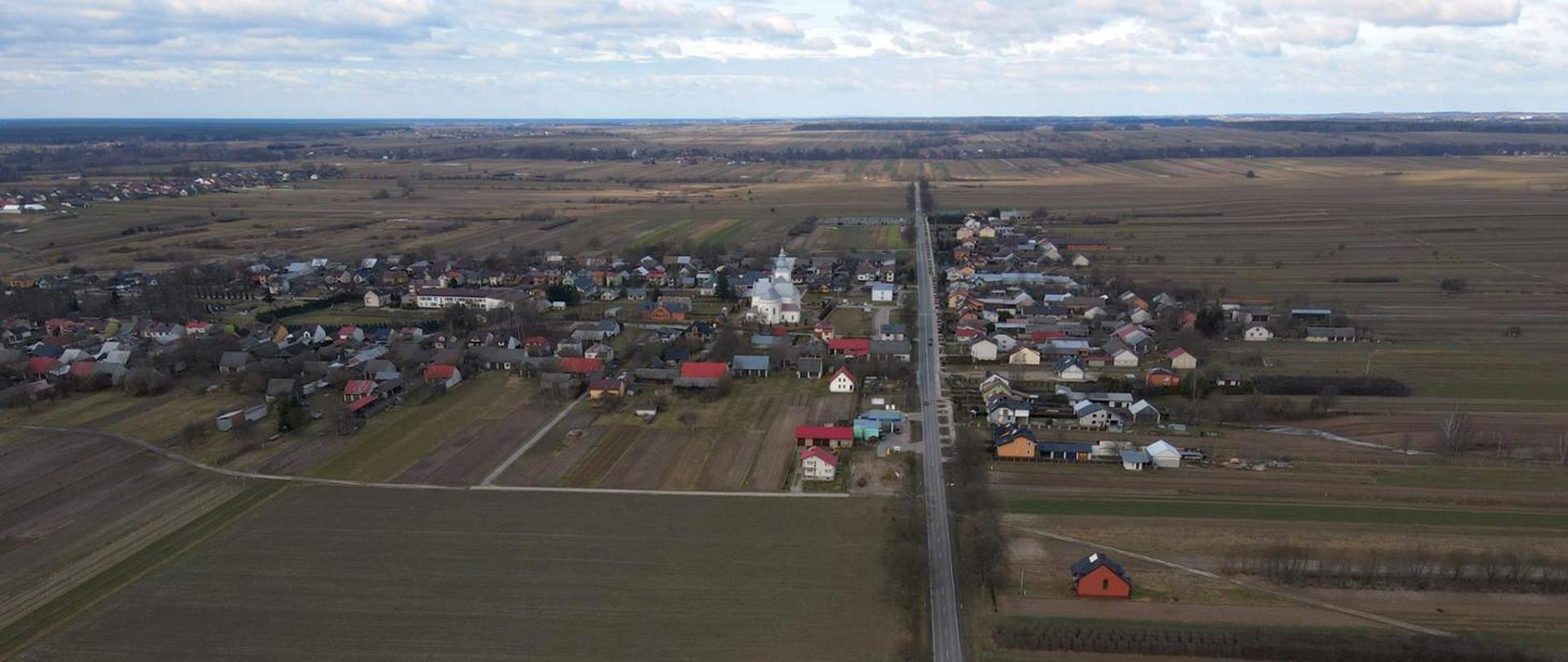 Widok z lotu ptaka na drogę biegnącą przez miejscowość. W tle widoczne pola.