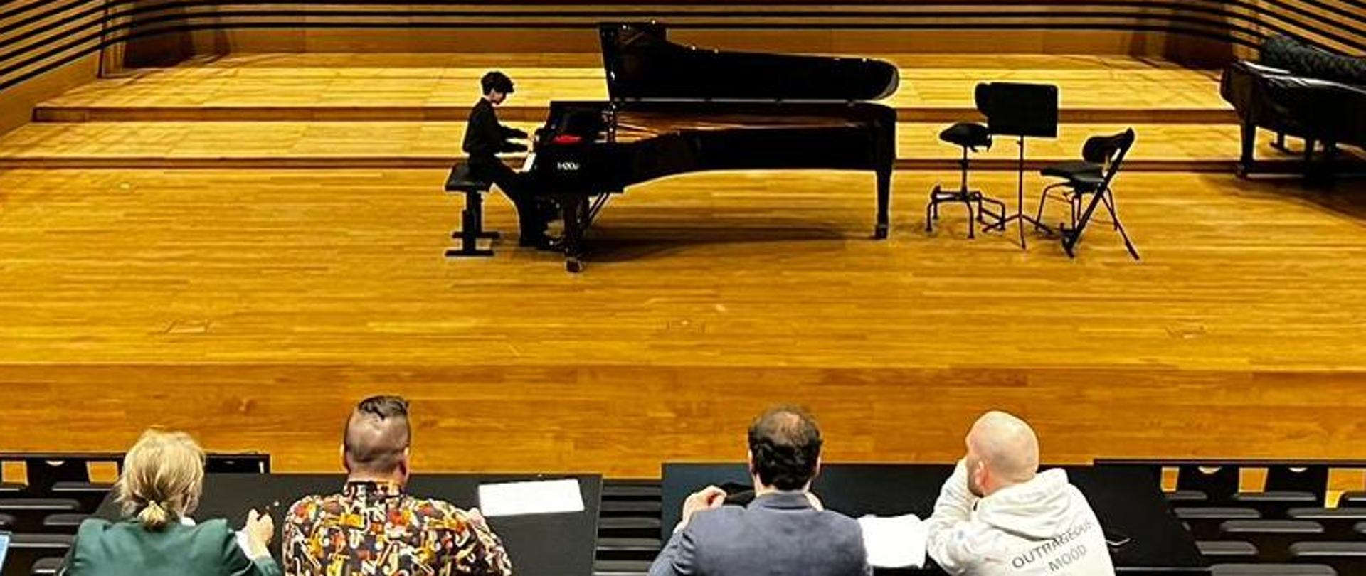 Chłopiec gra na fortepianie, z przodu widać id tyłu widownię i Jury.