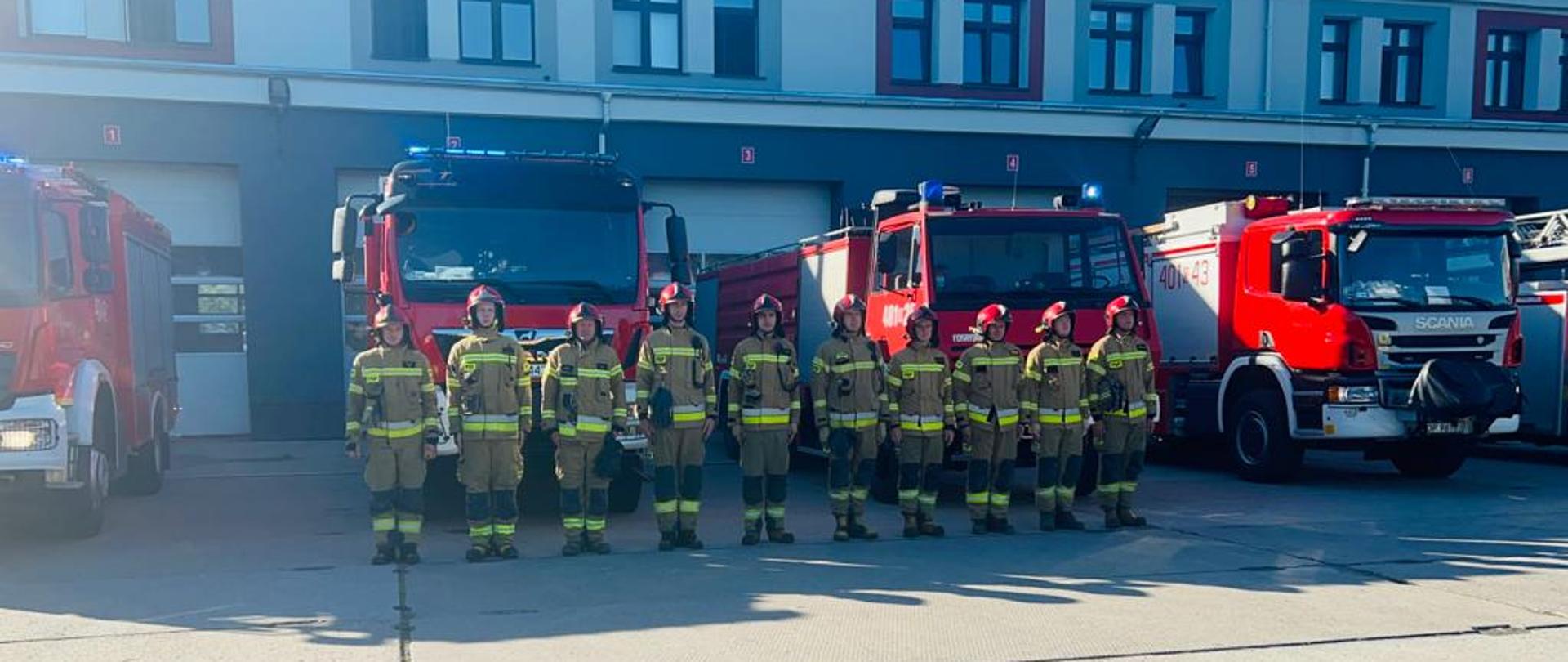 Minuta ciszy dla zmarłego strażaka - zdjęcie przedstawia strażaków JRG Brzeg przed siedzibą jednostki, w tle samochody pożarnicze.