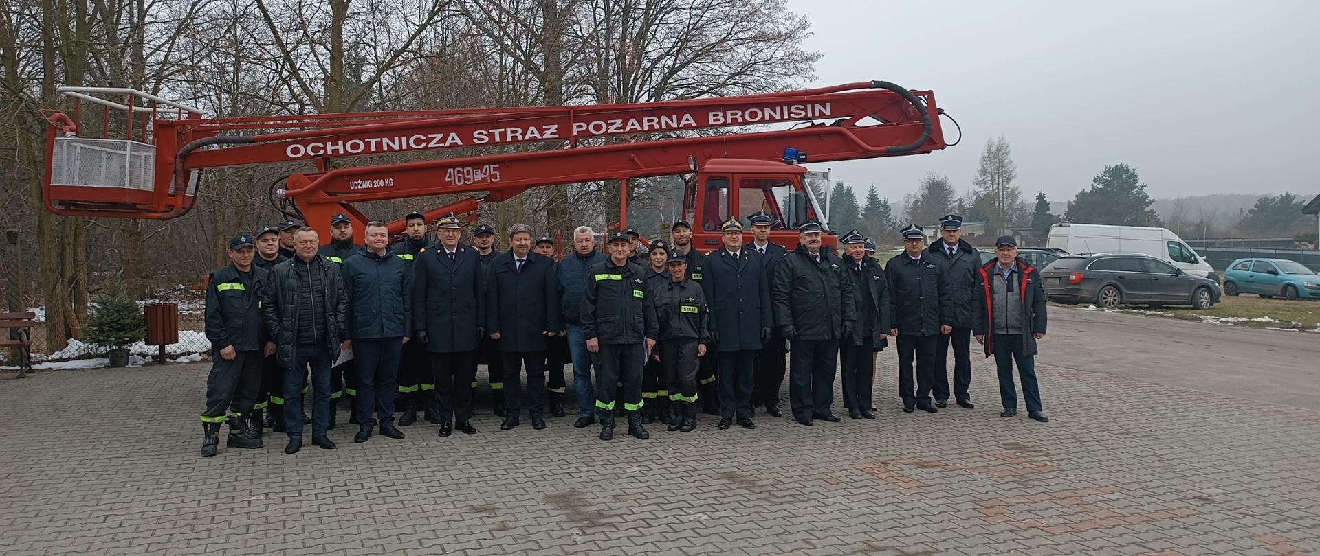 Zdjęcie przedstawia uczestników uroczystego przekazania SH 18 dla OSP w Adamowie, na tle samochodu SH 18