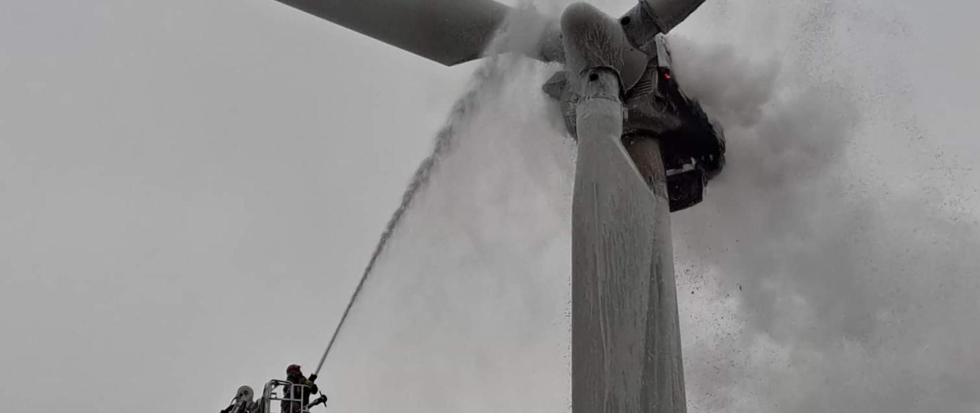 Na zdjęciu widać strażaka gaszącego z platformy podnośnika hydraulicznego pożar turbiny wiatrowej przy użyciu prądu gaśniczego.