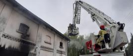 Budynek gospodarczy, okocone wejście, ratownicy w koszu podnośnika hydraulicznego PSP oraz operator tego podnośnika 