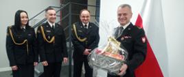 Zdjęcie przedstawia funkcjonariuszy Komendy Powiatowej Państwowej Straży Pożarnej w Człuchowie wręczających upominek przechodzącemu na zaopatrzenie emerytalne bryg. Piotrowi Głodowskiemu.