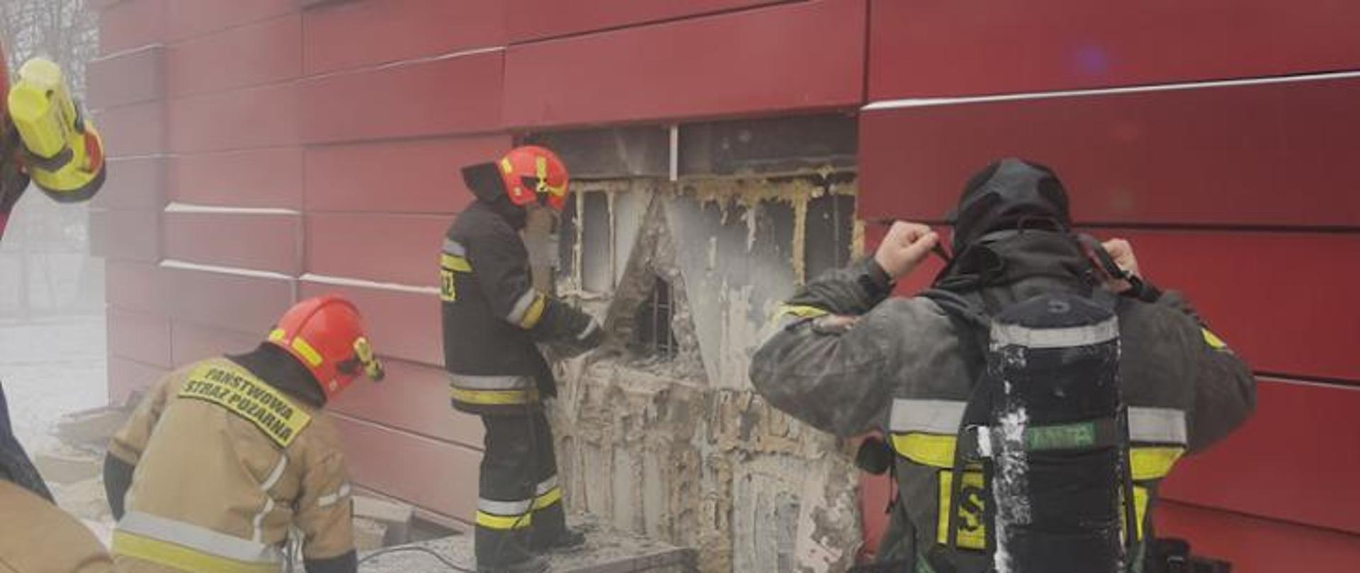 Strażacy wykonują otwór w ścianie budynku